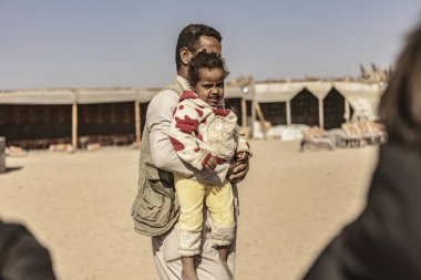 Marsa alam, 9 Şubat 2025: Bedevi bir baba küçük kızını Marsa Alam, Mısır 'da bir çöl kampında taşıyor, sevgi ve özeni ifade ediyor.