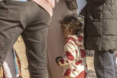 Marsa alam, Mısır 9 Şubat 2025: Marsa Alam, Mısır 'da bir çöl mülteci kampında yetişkinlerin yanında duran üzgün çocuk, elinde küçük bir nesne tutuyor.