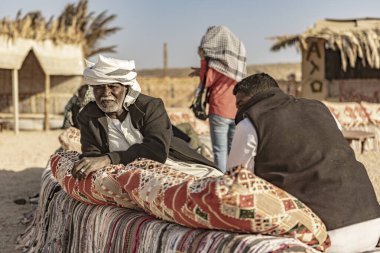 Marsa alam, Mısır 9 Şubat 2025: Marsa alam, Mısır 'da bir çöl kampında renkli yastıklarda dinlenen iki bedevi adam, huzurlu atmosferin tadını çıkarıyorlar.