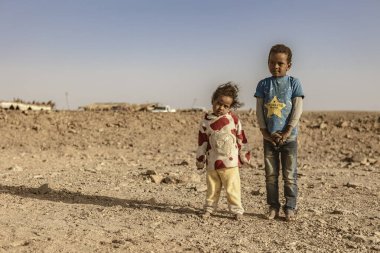 Marsa alam, Mısır 9 Şubat 2025: Marsa alam, Mısır 'da ıssız, kayalık bir çöl manzarasında duran iki çıplak ayaklı çocuk, yoksulluk ve yer değiştirme zorluklarını vurguluyor.