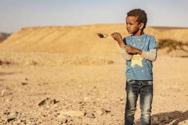 Marsa alam, Mısır 9 Şubat 2025: Meraklı genç çocuk Marsa alam çölünde bir bitki tutuyor, Mısır, gün ışığı altında kurak araziyi keşfediyor