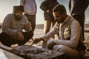 Marsa alam, Mısır 9 Şubat 2025: Bedevi rehberleri geleneksel kahveyi metal bir kapta sıcak küllerin üzerine hazırlıyor, kültürlerini Marsa alam çölünde, Mısır 'da turistlerle paylaşıyor.