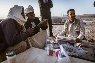 Marsa alam, Mısır 9 Şubat 2025: Geleneksel giysiler giyen bedeviler bir masanın etrafında oturmuş, Marsa Alam, Mısır çöllerinde sohbet ediyorlar.