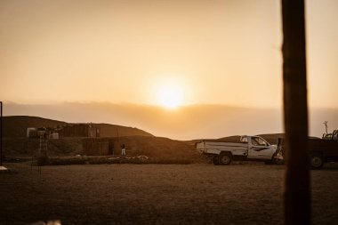 Marsa alam, 9 Şubat 2025: Mısır 'daki Marsa alam çölünde çarpıcı bir gün batımı, bir kamyonet ve basit konutları aydınlatarak, uzak çöl yaşamının özünü yakalıyor.