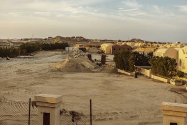 Marsa alam, Mısır 9 Şubat 2025: Kum ve moloz yığınları, sıcak bir günbatımı gökyüzü altında Marsa alam, Mısır 'da geleneksel kubbeli binaların arasında genişleyen bir inşaat alanı.