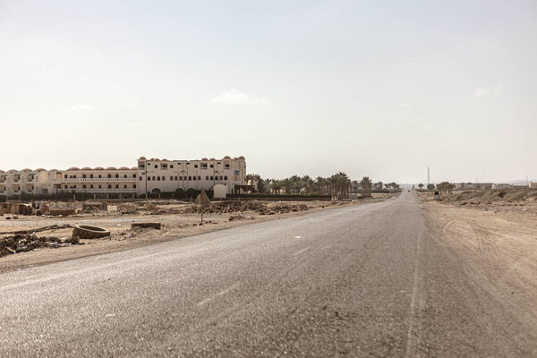 Марса алам, Египет 9 февраля 2025 года: пустынная асфальтовая дорога, протянувшаяся через пустынный ландшафт, ведущая к недостроенным, заброшенным зданиям в Марса алам, Египет