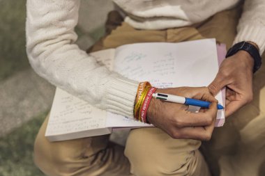 Torino, İtalya, 22 Ocak 2025: Bir basın toplantısı veya toplantı sırasında not defterine notlar yazan bir gazetecinin yakın çekimi, farkındalık bilezikleri takıyor