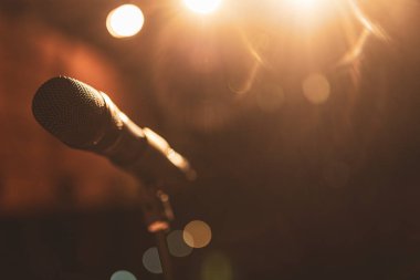 Sahnede sıcak ışık altında profesyonel mikrofon, bir şarkıcı veya konuşmacının konser veya etkinlikte sahne almasına hazır.