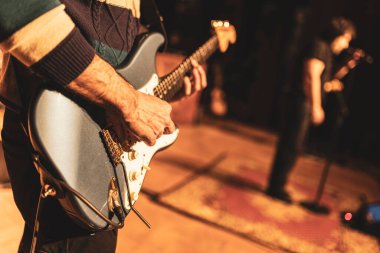 Sahnede canlı performans sırasında elektro gitar çalan bir müzisyenin yakın çekim görüntüsü seyirciyi büyülüyor.