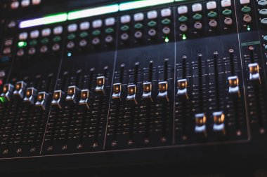 Profesyonel bir kayıt stüdyosundaki ses seviyelerini ayarlamak için kullanılan faders ve düğmeleri vurgulayan bir karıştırma konsolunun yakın çekimi