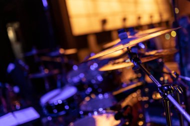 Canlı müzik performansı sırasında canlı ve atmosferik bir sahne yaratan, mor ve turuncu sahne ışıklarıyla yıkanmış bir zil ve davul setinin yakın çekimi