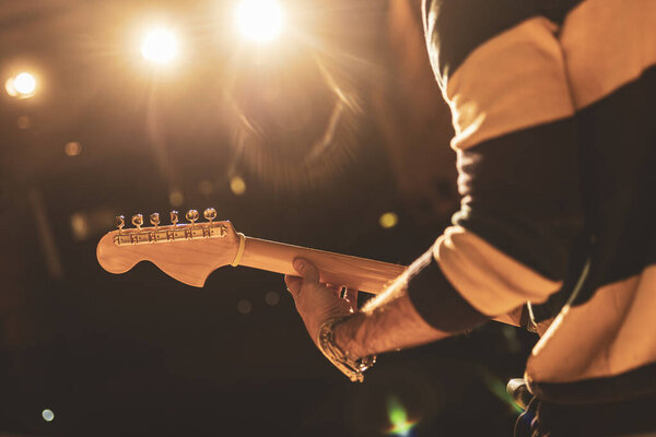 Close-up of a guitarist's hands playing electric guitar on a brightly lit stage, creating a captivating musical atmosphere