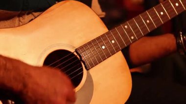 Yetenekli gitarist kusursuz parmak hareketleri ile karmaşık akustik gitar akorları yapıyor, sıcak ve samimi ışıklandırmada melodik sesler yaratıyor.