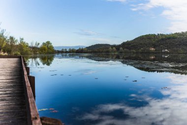 İtalya 'daki Fimon Gölü' nün huzur dolu güzelliğini gösteren sakin bir manzara. Mavi gökyüzünün altındaki sakin, yansıtıcı sulara uzanan ahşap bir iskele.