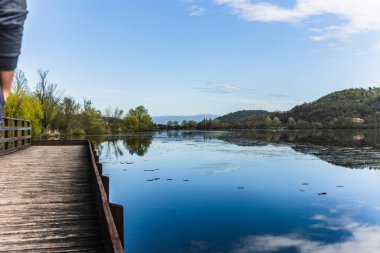 Sakin sular gökyüzünü ve etrafını çevreleyen tepeleri yansıtıyor. Fimon Gölü 'nde sakin bir manzara yaratıyor. Yıpranmış bir ahşap iskeleden ulaşılabilir.