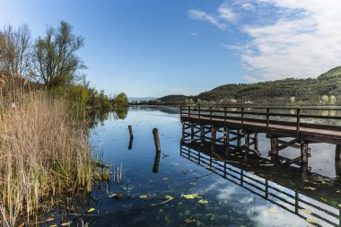 Fimon Gölü 'nün sakin sularına uzanan ahşap iskelenin sakin manzarası mavi gökyüzünü ve doğayı yansıtıyor.