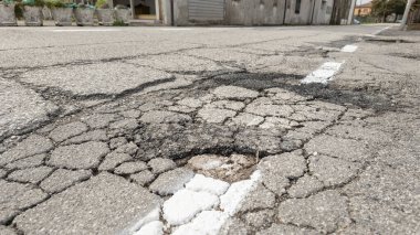 Belirsiz asfalt yol yüzeyinde çatlaklar ve çukurlar görülüyor, yol bakımı ve onarım ihtiyacı vurgulanıyor