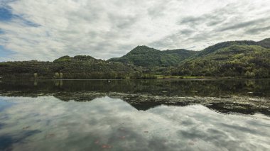 Sakin su yeşil tepeleri ve Fimon Gölü 'ndeki bulutlu gökyüzünü yansıtıyor. Vicenza, İtalya' da huzurlu bir bahar gününde.