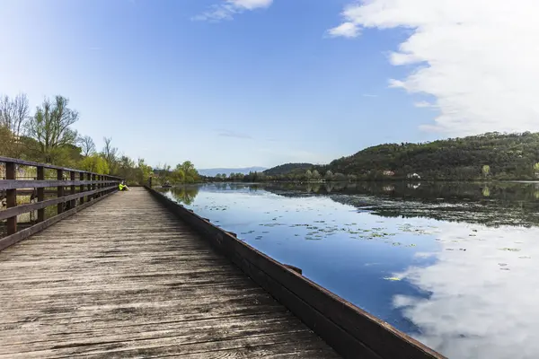 Uzun ahşap iskele Fimon gölünün sakin sularına uzanıyor, gökyüzünü ve etrafındaki tepeleri yansıtıyor, huzurlu bir manzara yaratıyor.