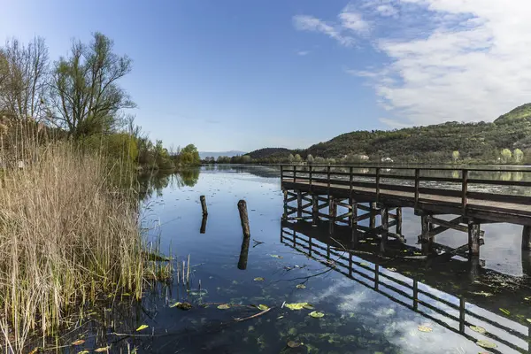 Fimon Gölü 'nün sakin sularına uzanan ahşap iskelenin sakin manzarası mavi gökyüzünü ve doğayı yansıtıyor.