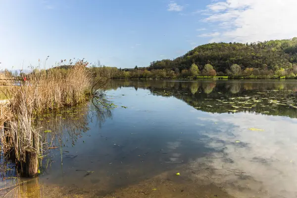 Fimon Gölü 'nün sakin suları Veneto, İtalya' da sakin bir bahar gününde yemyeşil tepelerin ve mavi gökyüzünün çevresini yansıtıyor.
