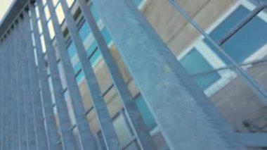 Metal parmaklıklar geometrik desen oluşturarak çok katlı bina cephesini kısmen engelliyor, pencere ızgarası ve kentsel perspektifle mimari ayrıntıları gösteriyor
