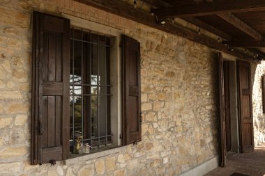 Metal parmaklıklarla aydınlatan güneş ışığı ve geleneksel İtalyan çiftlik evinin taş duvarında açık ahşap panjurlar.