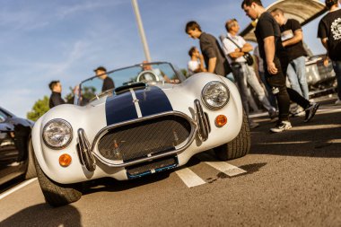 Roma, İtalya 4 Mayıs 2025: Beyaz ve mavi Shelby Kobra 427 bir araba toplantısı sırasında mekanik ve ziyaretçilerle park etmiş.