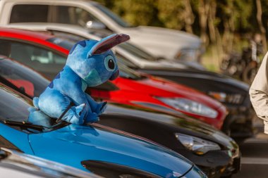 Roma, İtalya 4 Mayıs 2025: Disney 'in lilo & dikişinden dikişe benzeyen mavi peluş oyuncak bir otoparkta mavi bir arabanın kaputuna tünemiş ve arka planda diğer araçlar görülebiliyor.