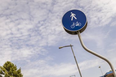 Yayalar ve bisikletler için yuvarlak mavi yol işareti bulutlu bir gökyüzünün altında özel bir şerit olduğunu gösteriyor.