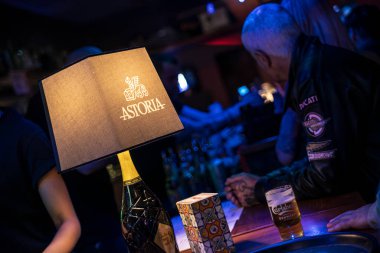 Roma, İtalya 4 Mayıs 2025: Astoria markalı lamba bir şişe Astoria şarabı ve bir bardak Carlsberg birasını gece bir bar tezgahında aydınlatıyor.