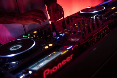 Roma, İtalya, 4 Mayıs 2025: DJ 'in elleri, öncü bir DJ kontrolörünün düğmelerini ve faderilerini manipüle ederek canlı bir gece kulübü atmosferinde elektronik müzik yaratıyor.