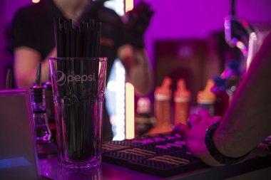 Roma, İtalya, 4 Mayıs 2025: Pepsi damgalı bir bardakta siyah pipetler bir barmen barın tezgahında otururken barmen canlı, neon ışıklı bir ortamda içki hazırlıyor.