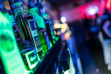 Roma, İtalya, 4 Mayıs 2025: yeşil likör şişeleri bir bar rafında aydınlanıyor, hareketli bir gece kulübünde canlı bir atmosfer yaratıyor.