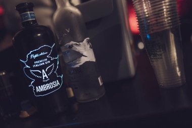 Roma, İtalya, 4 Mayıs 2025: Gri bir kaz votka şişesi ve plastik bardakların yanında bir barın üzerinde parlayan ambrosia cin şişesinin yakın çekimi