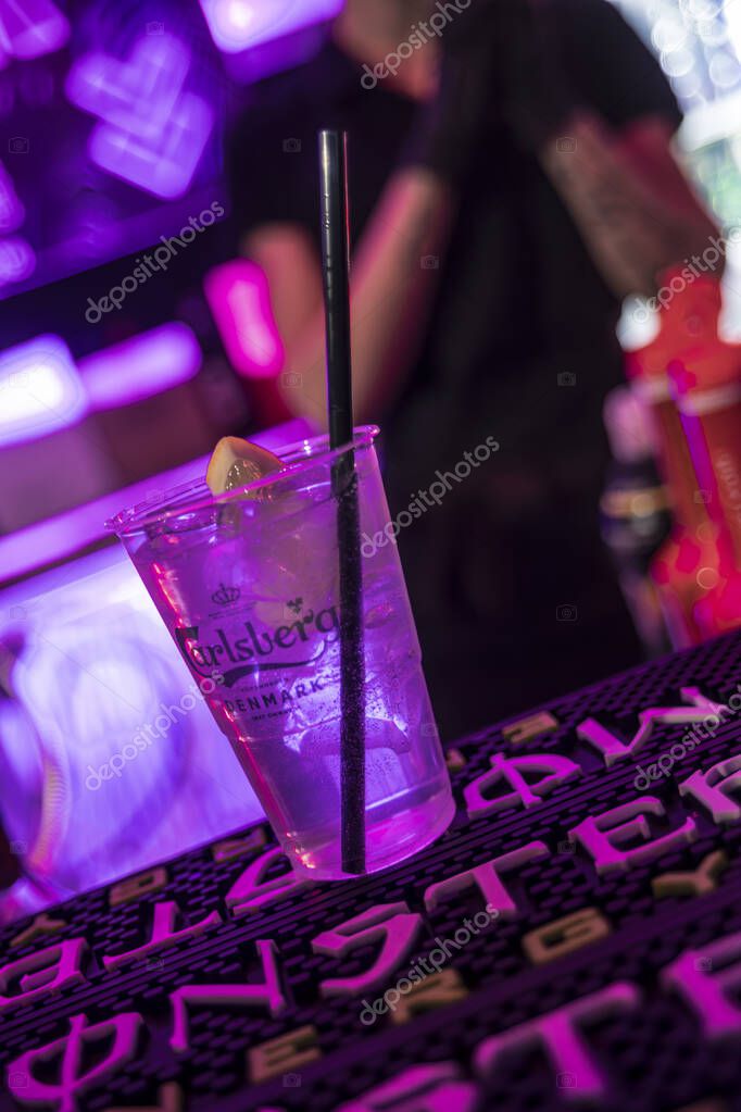 Rome, italy 4 may 2025: plastic cup with carlsberg beer, ice, lemon and black straw on bar mat in purple-lit nightclub