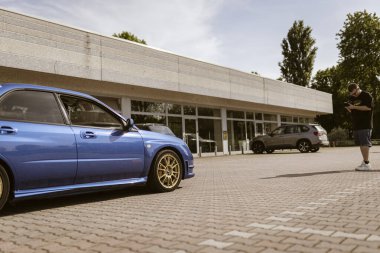 Milan, İtalya 4 Haziran 2025, bir fotoğrafçı modern bir binanın önündeki otoparkta mavi akortlu bir spor arabanın fotoğraflarını çekiyor.