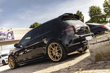 Milan, İtalya, 4 Haziran 2025, özelleştirilmiş siyah Volkswagen golf gti, altın jantlar, açık bir gökyüzünün altındaki asfalt bir alanda park edilmiş