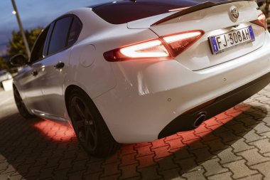 Milan, İtalya 4 Haziran 2025, gösterişli beyaz alfa romeo giulia, gece yarısı asfaltlı bir yüzeye parlayan parlak kırmızı alfa.