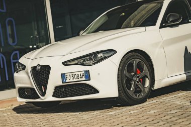 Milan, İtalya 4 Haziran 2025, zarif beyaz alfa Romeo Giulia parke taşlı bir caddeye park edilmiş, gösterişli tasarımı ve spor özellikleri sergileniyor.