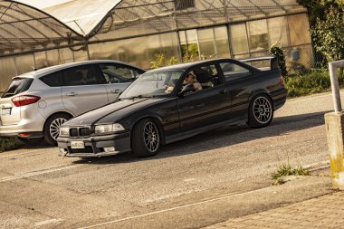 Milan, İtalya 4 Haziran 2025, güneşli bir günde, muhtemelen bir araba yarışından sonra, akort edilmiş siyah BMW E36 kullanan bir kadın.