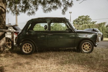 Roma, İtalya, 17 Haziran 2025, bir ağacın altında çimlere park etmiş klasik tasarımı ve altın jantlarını sergileyen klasik bir rover mini Cooper 'ın yan görüntüsü.