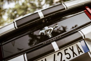 Roma, İtalya, 17 Haziran 2025, krom Ford Mustang logosu siyah yarış şeritlerinde dörtnala giden bir at, Amerikan kas ve hızının özünü yakalıyor.