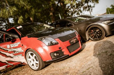 Roma, İtalya, 17 Haziran 2025, özelleştirilmiş kırmızı Suzuki Swift spor diğer ayarlanmış arabaların yanına park edilmiş açık kapılı ağaç gölgesinin altındaki otoparkta.