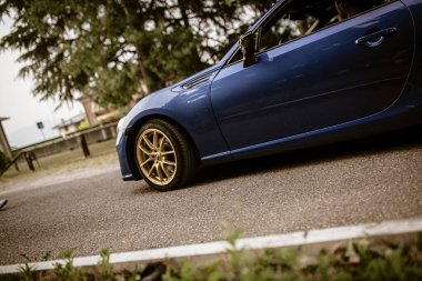 Roma, İtalya, 17 Haziran 2025, şık mavi spor araba asfaltlı bir yolda ilerliyor, altın jantlarını ve parlak tasarımlarını sergiliyor.