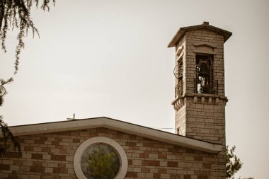 İçinde metal çan olan tuğla kilise çan kulesi, dairesel pencereli ve çatısında çapraz duran ana binanın üzerinde duruyor.