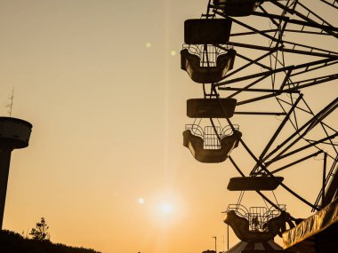 Dönme dolap gondolları eğlence parkında güzel bir günbatımına karşı siluetlendi. Su kulesi nostaljik atmosfere katkı sağladı.