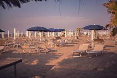Chioggia, İtalya 'da kumlu sahilde duran boş güneşlikler ve plaj şemsiyeleri huzurlu bir yaz ortamı yaratıyor.