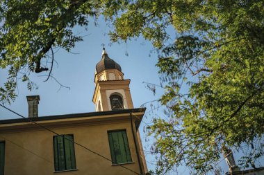 Roma, İtalya 'da yemyeşil ağaçlarla çevrili yerleşim yerinin tepesinden yükselen bir kilise kulesinin alçak açılı görüntüsü.