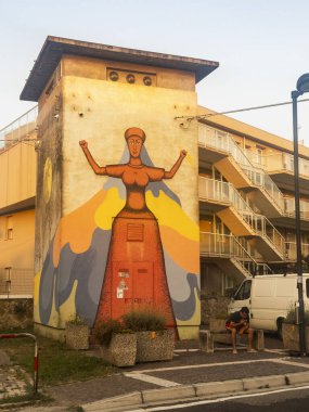 Rosolina Mare, İtalya, 21 Haziran 2025, ateş ve su tutan, denge ve gücü temsil eden bir kadının yer aldığı sokak sanatı, yerleşim alanındaki bir elektrik kulübesini süslüyor.